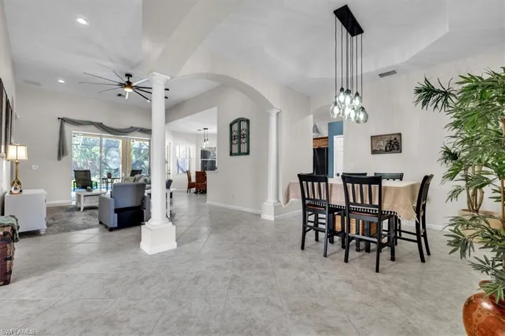Dining area featuring ornate columns, arched walkways, a ceiling fan, and light tile patterned flooring