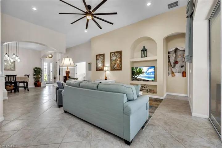 Living room with built in features, arched walkways, ceiling fan, light tile patterned floors, and a chandelier