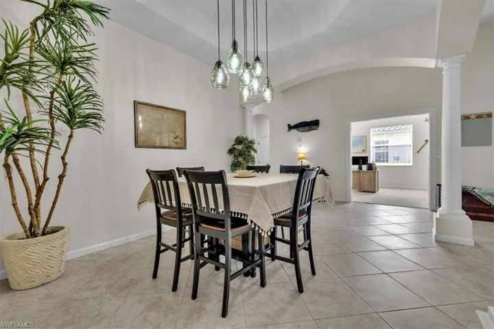 Dining area with ornate columns, arched walkways, light tile patterned floors, and a high ceiling