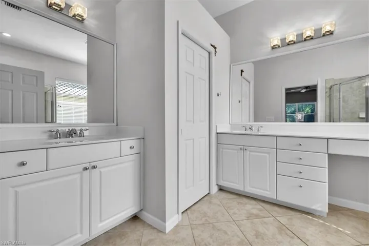 Full bath with two vanities, a shower stall, and light tile patterned flooring