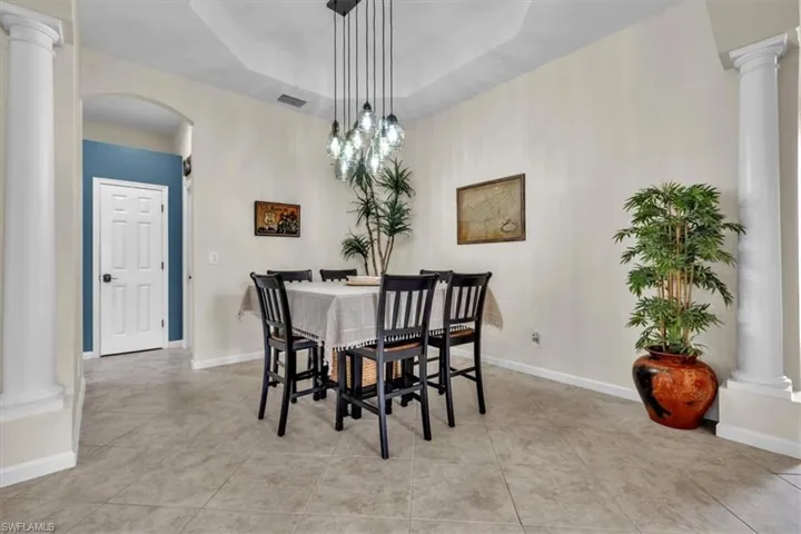 Dining space featuring ornate columns, arched walkways, a raised ceiling, and light tile patterned floors
