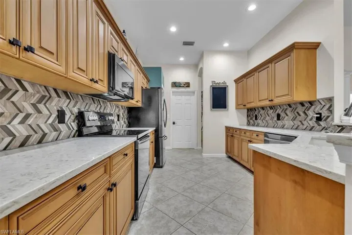 Kitchen featuring stainless steel appliances, light stone countertops, a peninsula, light tile patterned floors, and decorative backsplash