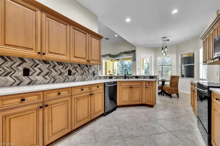 Kitchen featuring decorative backsplash, a peninsula, black appliances, light tile patterned floors, and wood finish cabinetry