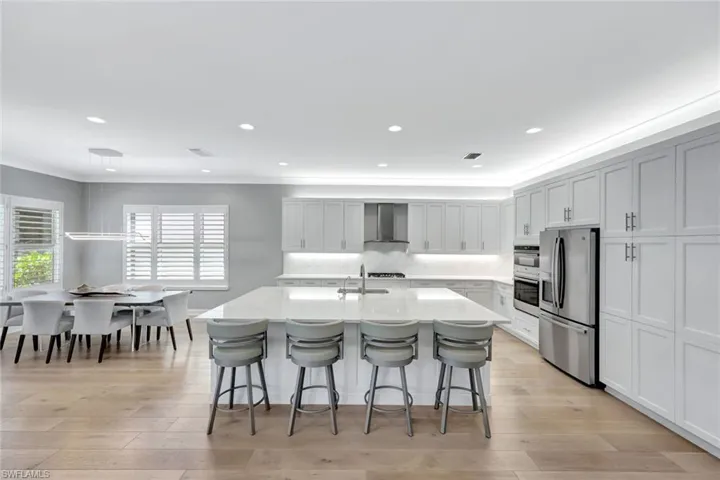 Kitchen featuring light wood-style flooring, stainless steel appliances, a breakfast bar area, and wall chimney range hood