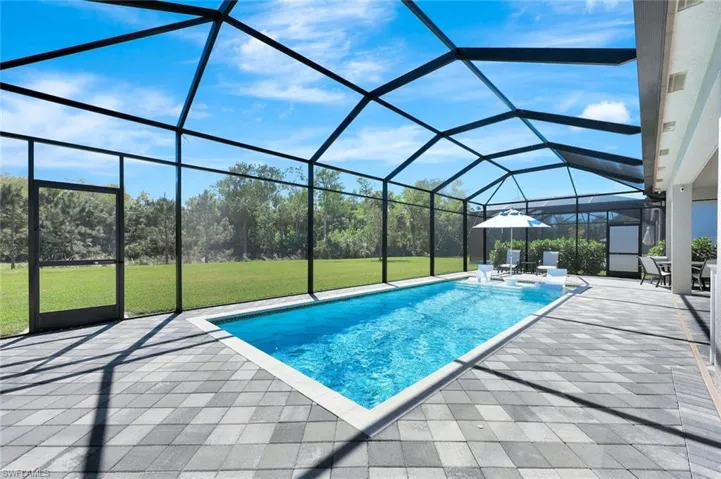 Outdoor pool with glass enclosure, a patio, and a lawn