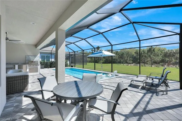 View of patio / terrace featuring glass enclosure, exterior kitchen, a ceiling fan, and an outdoor pool