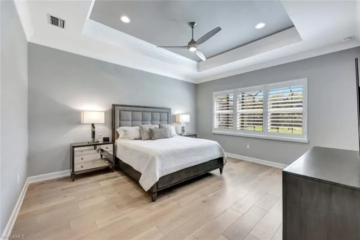 Bedroom featuring a tray ceiling, baseboards, and light wood-style flooring