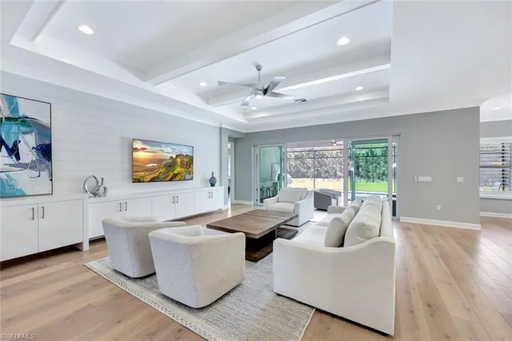 Living room with a tray ceiling, recessed lighting, light wood-style floors, and baseboards