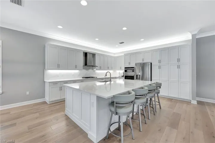 Kitchen with a breakfast bar area, light wood finished floors, a sink, stainless steel appliances, and wall chimney range hood