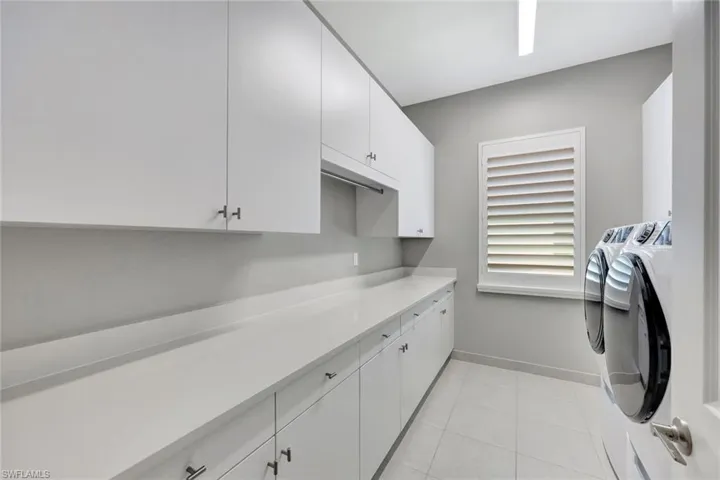 Clothes washing area with light tile patterned floors, baseboards, cabinet space, and washing machine and dryer
