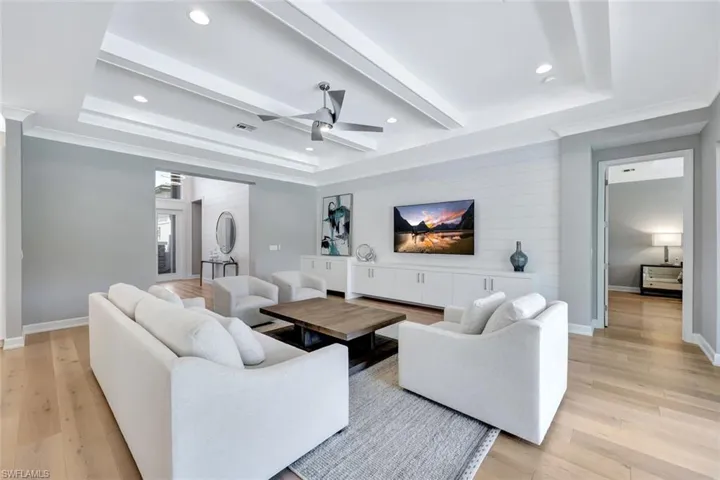 Living area with a raised ceiling, light wood-style flooring, beamed ceiling, and baseboards