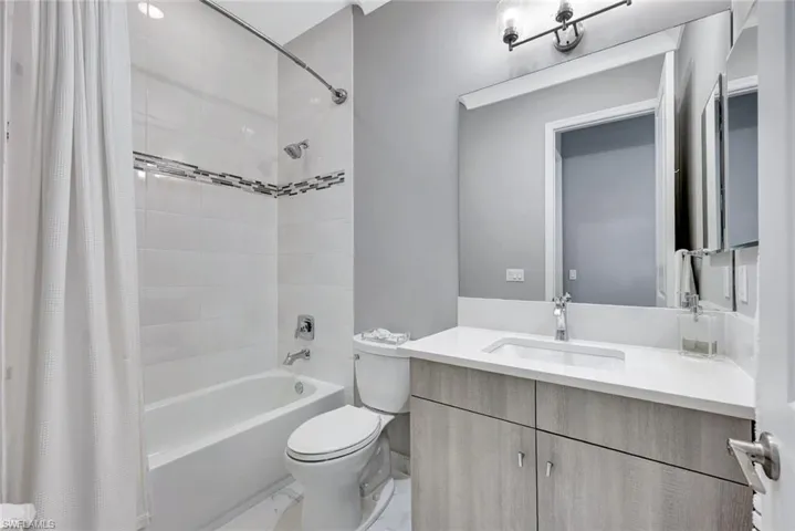 Bathroom featuring vanity, shower / bath combination with curtain, toilet, and marble finish floor