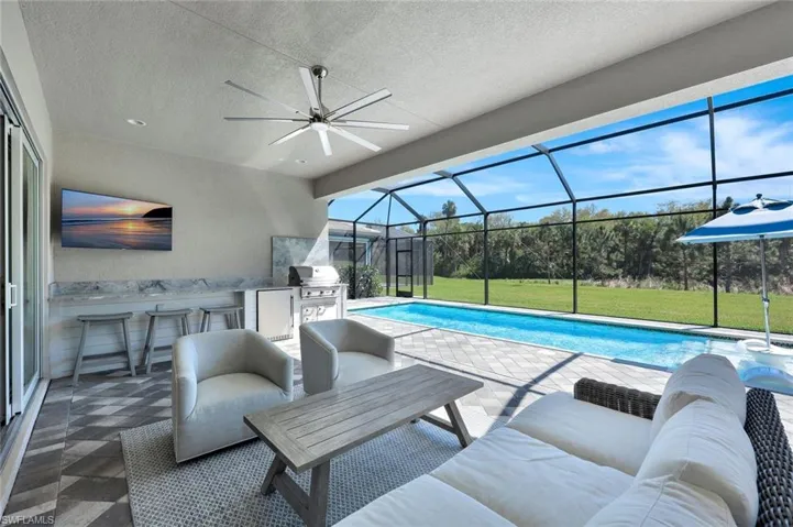 Pool featuring glass enclosure, a lawn, area for grilling, a ceiling fan, and a patio