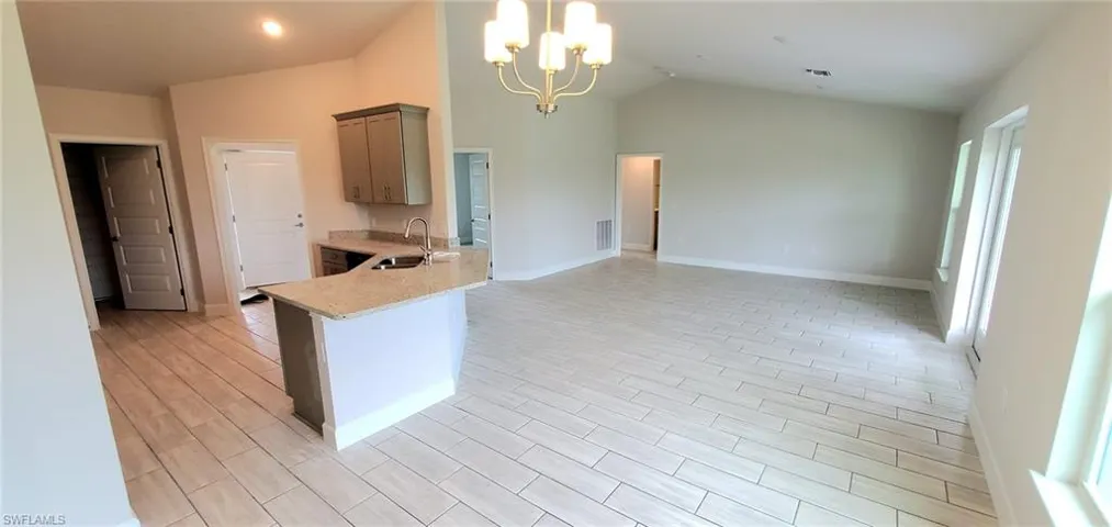 Kitchen featuring sink, hanging light fixtures, light stone countertops, lofted ceiling, and a chandelier
