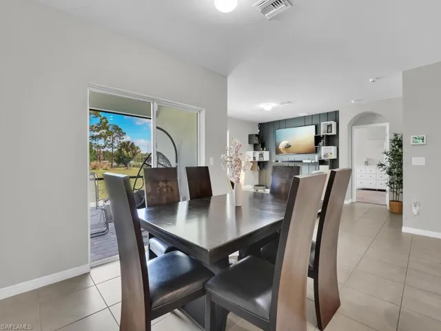 Dining room with light tile patterned floors, arched walkways, visible vents, and baseboards