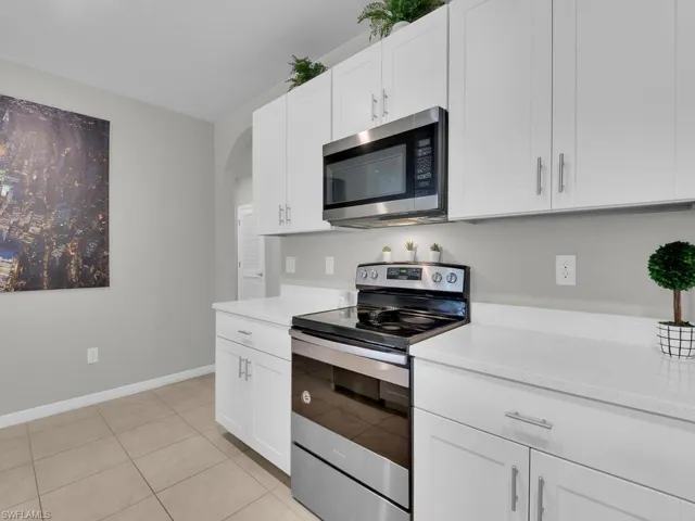 Kitchen with baseboards, arched walkways, stainless steel appliances, light countertops, and white cabinets