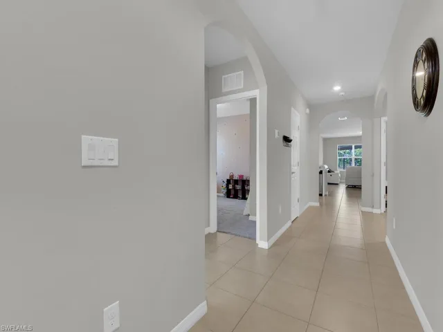 Hallway with visible vents, baseboards, arched walkways, and light tile patterned flooring