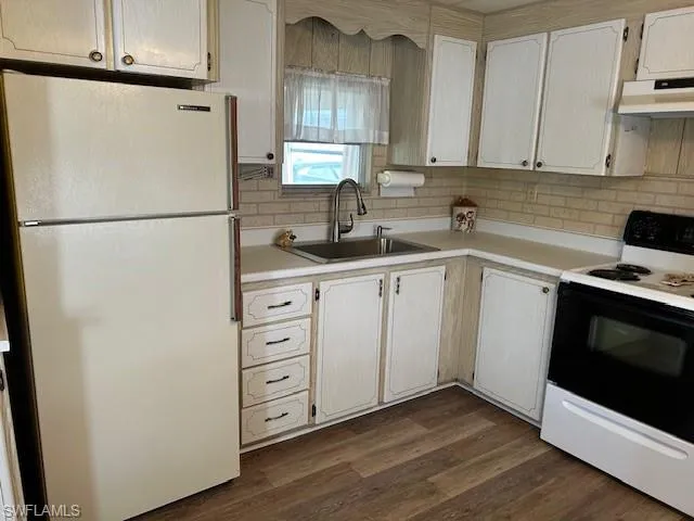 Kitchen with white appliances, under cabinet range hood, light countertops, and dark wood-style flooring