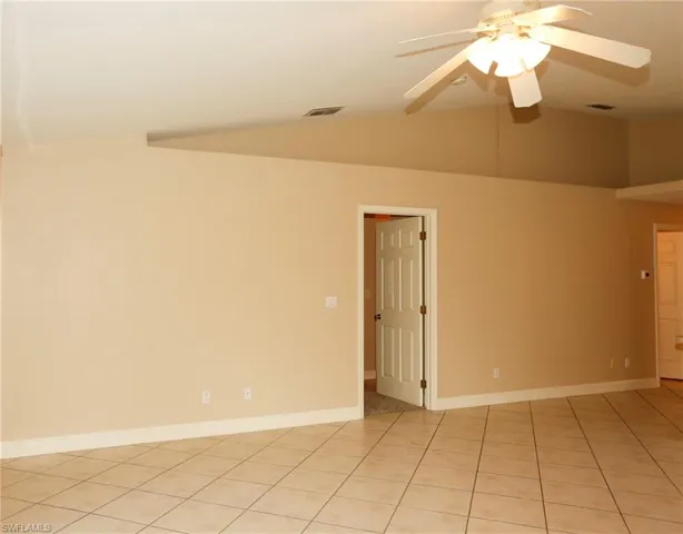 Spacious room featuring vaulted ceilings, a ceiling fan with integrated lighting, ceramic tile flooring, and neutral wall tones