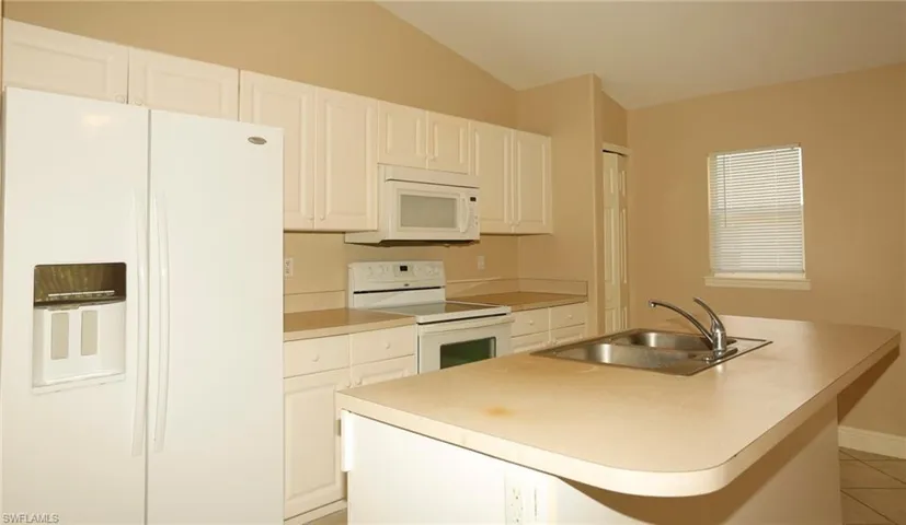 Kitchen featuring white cabinetry, light-toned countertops, a double basin sink with a chrome faucet, a white side-by-side refrigerator, and a white electric range with an overhead microwave