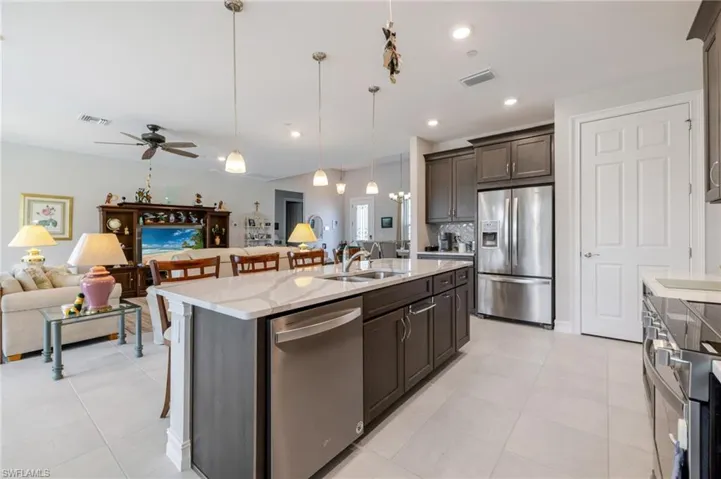 Kitchen featuring open floor plan, a breakfast bar area, dark brown cabinetry, appliances with stainless steel finishes, and decorative light fixtures