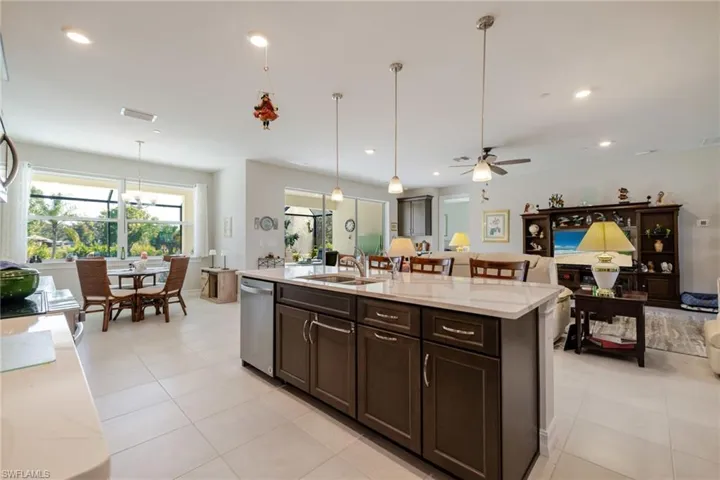 Kitchen featuring dark brown cabinetry, hanging light fixtures, light stone countertops, open floor plan, and a kitchen island with sink