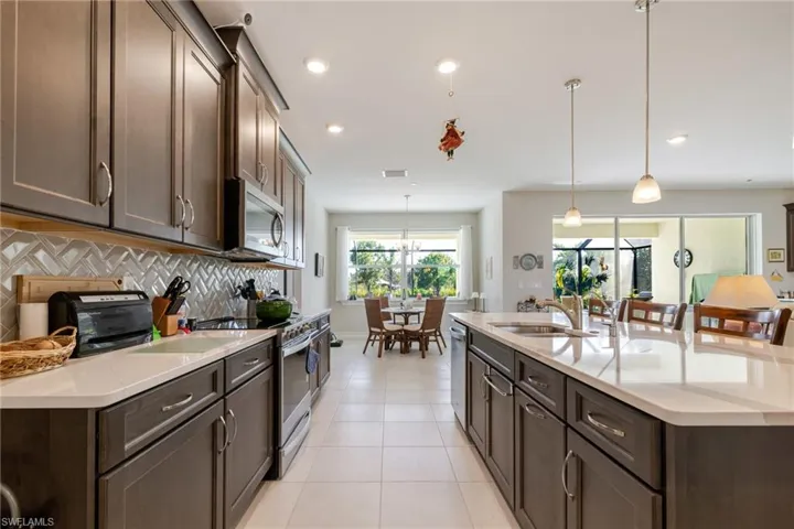 Kitchen with dark brown cabinetry, stainless steel appliances, decorative backsplash, hanging light fixtures, and light tile patterned flooring