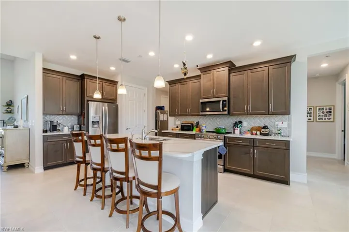 Kitchen featuring dark brown cabinets, a kitchen breakfast bar, appliances with stainless steel finishes, pendant lighting, and a center island with sink