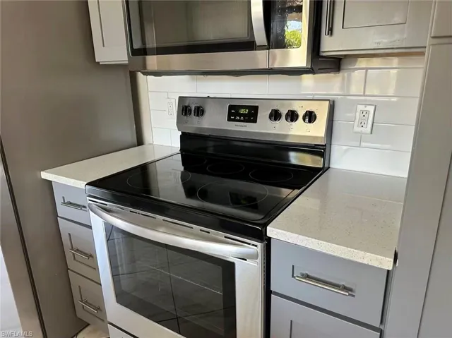 Kitchen featuring stainless steel appliances, light stone counters, gray cabinets, and tasteful backsplash