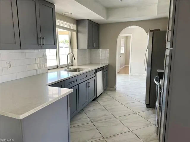 Kitchen featuring gray cabinetry, light stone countertops, tasteful backsplash, light marble finish flooring, and stainless steel appliances