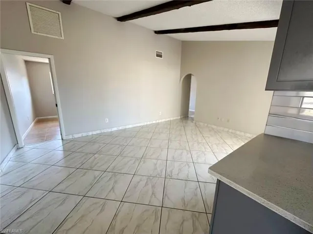 Unfurnished living room with arched walkways, beamed ceiling, and light marble finish flooring
