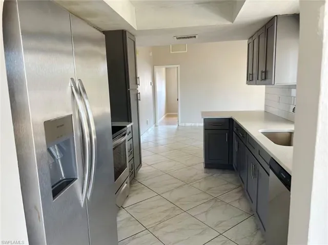 Kitchen featuring stainless steel appliances, light stone countertops, light marble finish floors, and backsplash