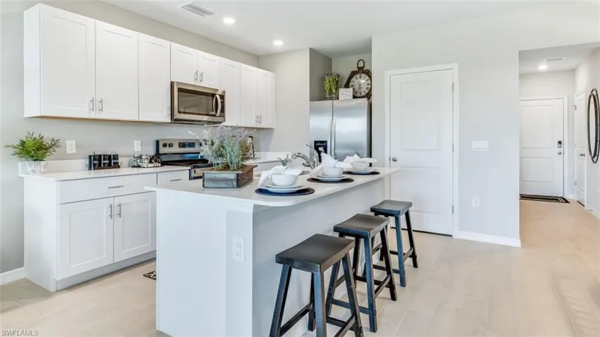 Kitchen featuring a breakfast bar, a center island with sink, light hardwood / wood-style floors, white cabinetry, and stainless steel appliances