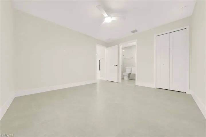 Unfurnished bedroom featuring concrete floors, ensuite bath, a ceiling fan, and a closet