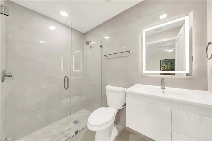 Full bath with vanity, a stall shower, tile walls, and recessed lighting