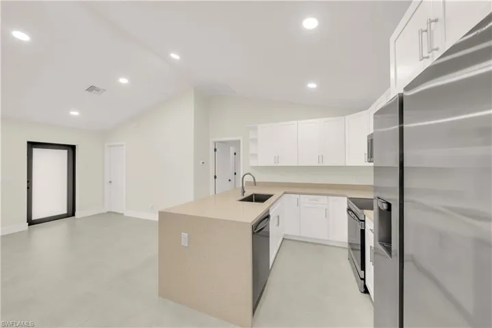 Kitchen with appliances with stainless steel finishes, a peninsula, white cabinetry, vaulted ceiling, and light stone countertops