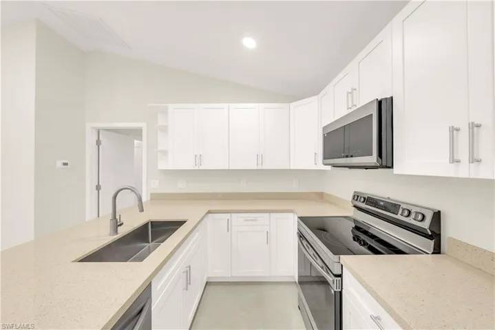 Kitchen featuring open shelves, stainless steel appliances, light stone countertops, white cabinets, and lofted ceiling