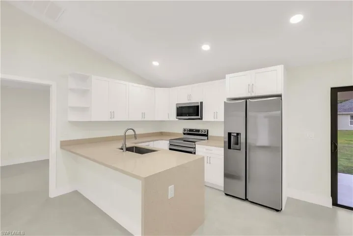Kitchen with open shelves, stainless steel appliances, white cabinetry, a peninsula, and light stone countertops