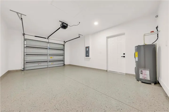 Garage with water heater, electric panel, and a garage door opener