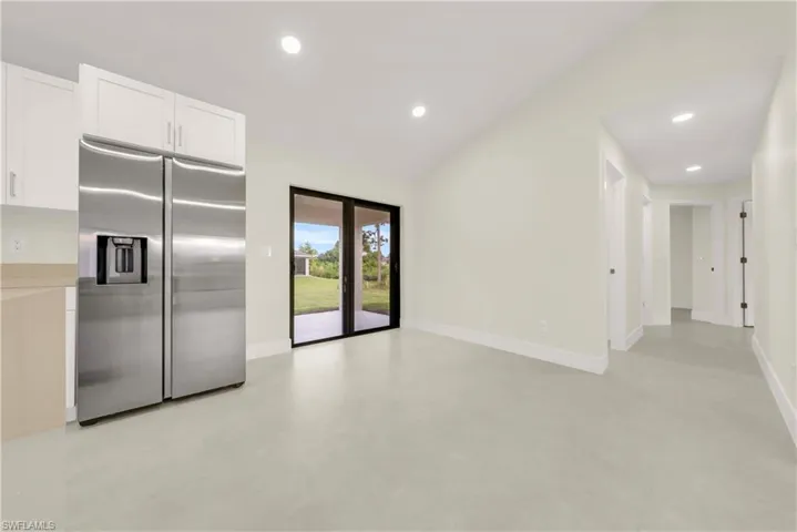 Kitchen featuring stainless steel refrigerator with ice dispenser, white cabinets, finished concrete floors, lofted ceiling, and recessed lighting