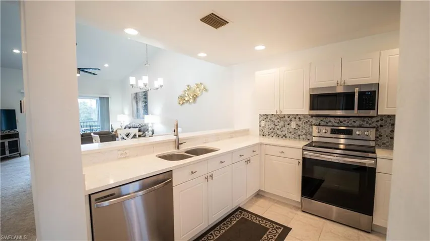 Kitchen with appliances with stainless steel finishes, white cabinetry, open floor plan, light stone countertops, and backsplash