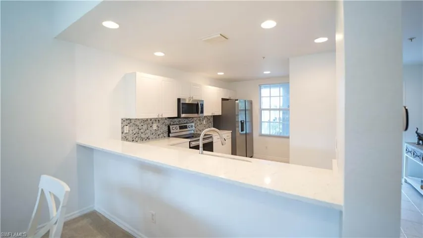 Kitchen featuring decorative backsplash, white cabinets, light stone countertops, stainless steel appliances, and recessed lighting