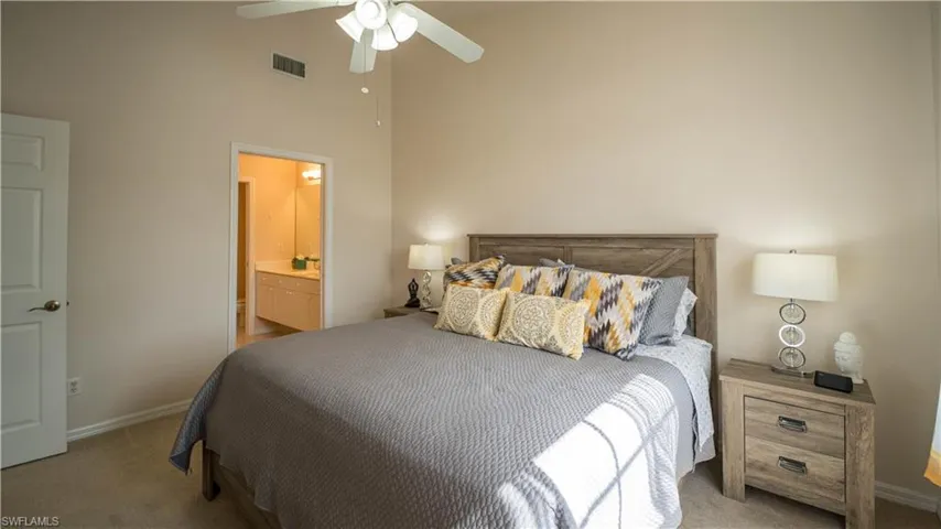 Bedroom with carpet flooring, high vaulted ceiling, ceiling fan, and ensuite bath