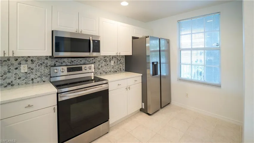 Kitchen featuring appliances with stainless steel finishes, backsplash, white cabinetry, light stone countertops, and recessed lighting