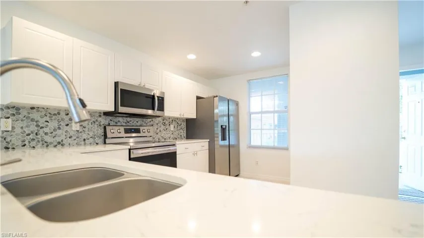 Kitchen featuring appliances with stainless steel finishes, white cabinetry, backsplash, light stone counters, and recessed lighting