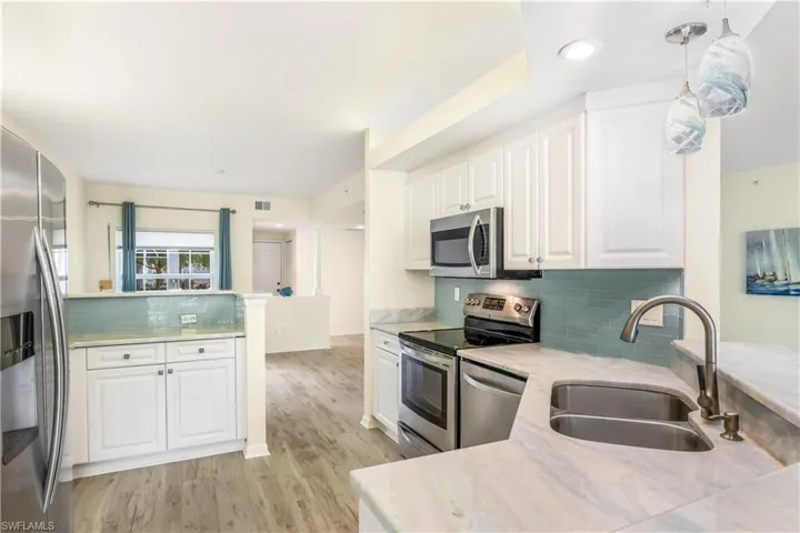 Kitchen featuring appliances with stainless steel finishes, white cabinets, marble counters, glass backsplash, dual stainless steel sink, decorative light fixtures, and new LTV flooring