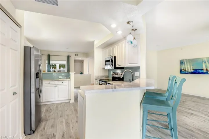 Kitchen featuring a breakfast bar area, stainless steel appliances, kitchen peninsula, new LTV flooring, white cabinetry, and marble counters