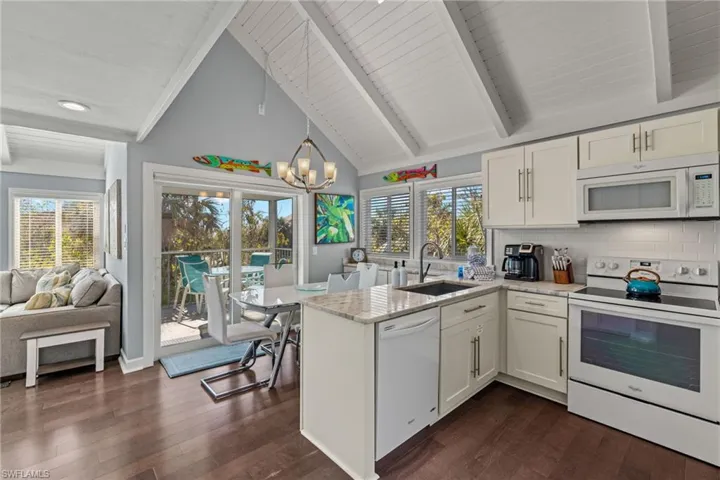 Kitchen with white appliances, sink, decorative backsplash, white cabinetry, and a chandelier