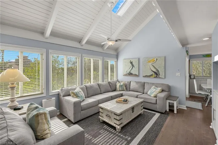 Living room featuring beam ceiling, a skylight, ceiling fan, dark hardwood / wood-style flooring, and high vaulted ceiling