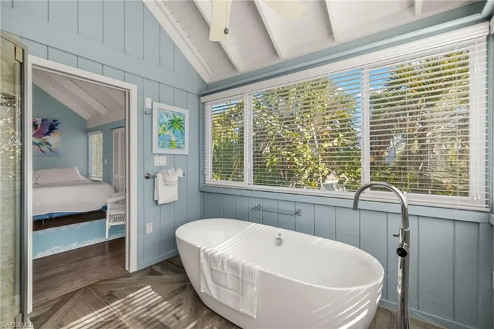 Bathroom with vaulted ceiling with beams, ceiling fan, a bath, and parquet flooring